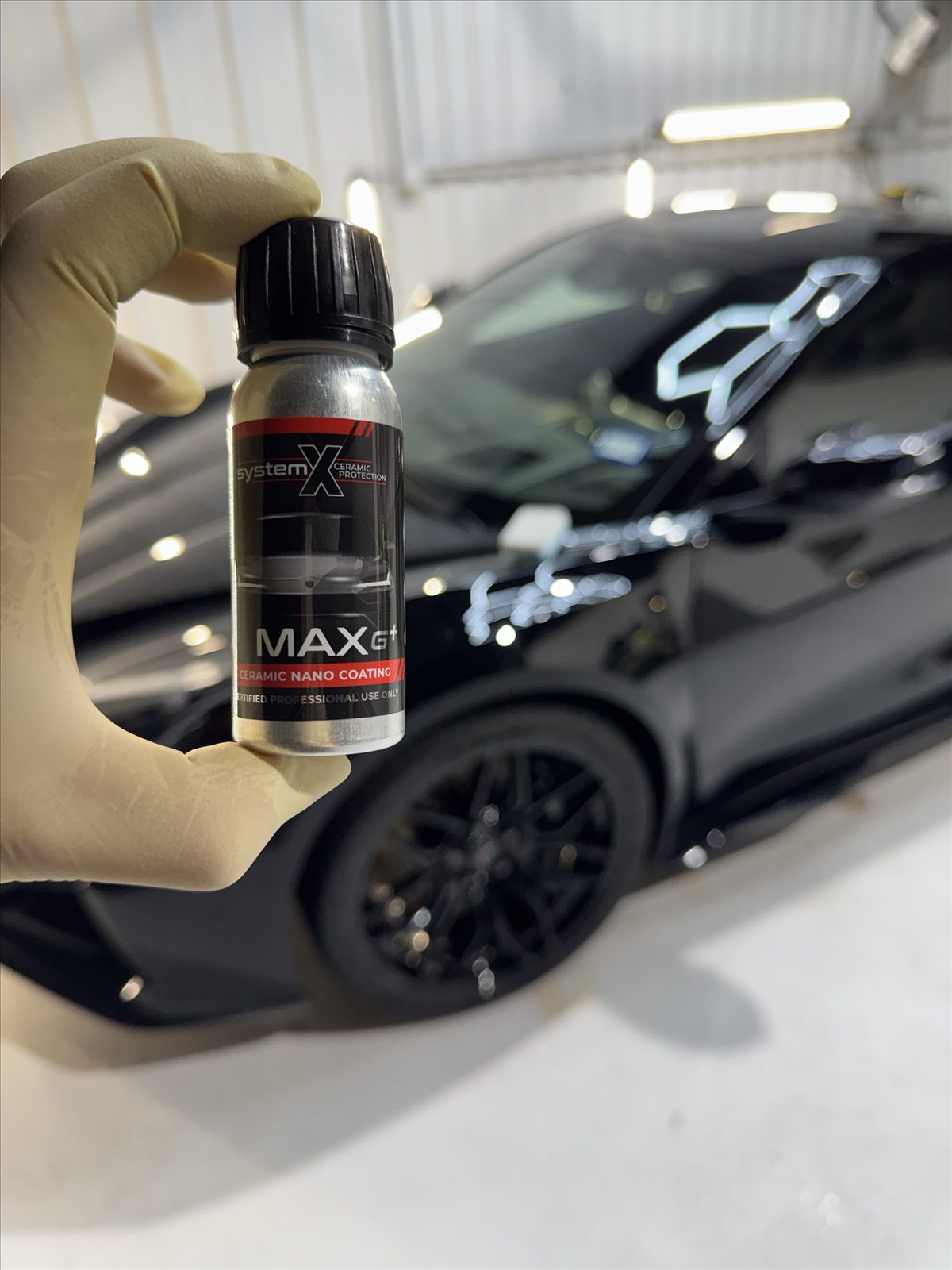 A bottle of System X MAX G+ ceramic nano coating, the car it is being applied to blurred behind it